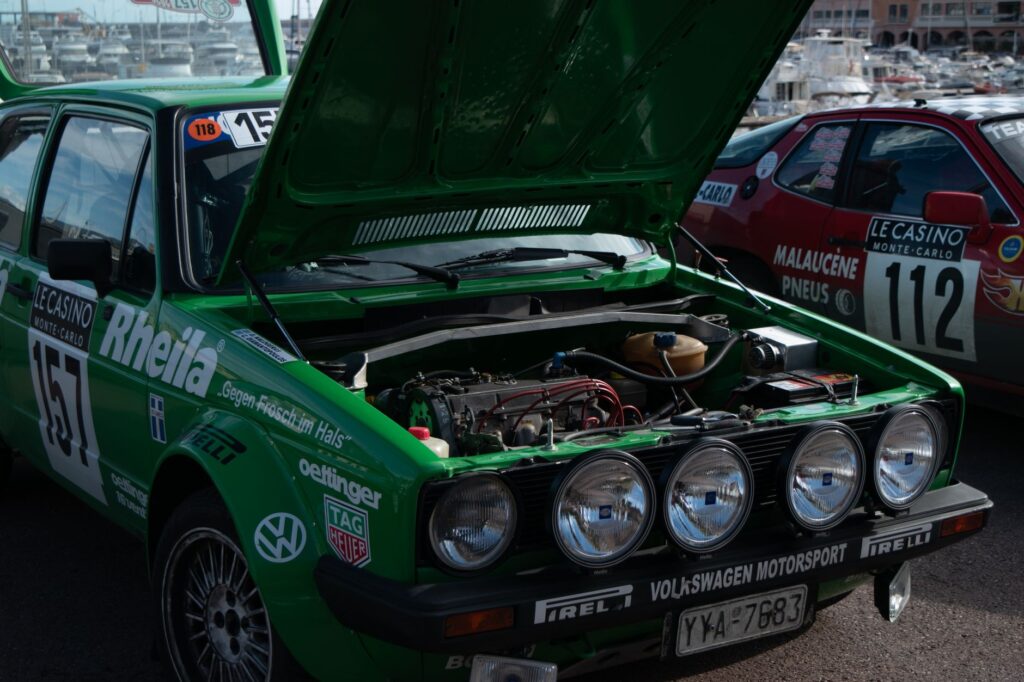 Green rally car with open hood, exposed engine at Monaco event.