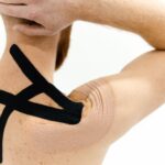 A man with kinesiology tape applied on his shoulder against a white background, showcasing physical therapy support.