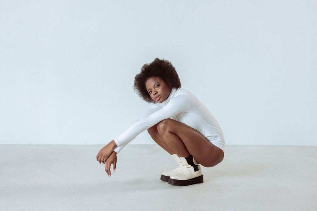 Elegant fashion portrait of a model crouching in a studio, highlighting modern style and afro hair.