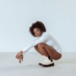 Elegant fashion portrait of a model crouching in a studio, highlighting modern style and afro hair.