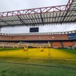 Wide-angle view of San Siro Stadium field, showcasing seating and lighting equipment inside the iconic venue.