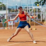 Dynamic shot of a female tennis player hitting a forehand on a clay court during a sunny day.