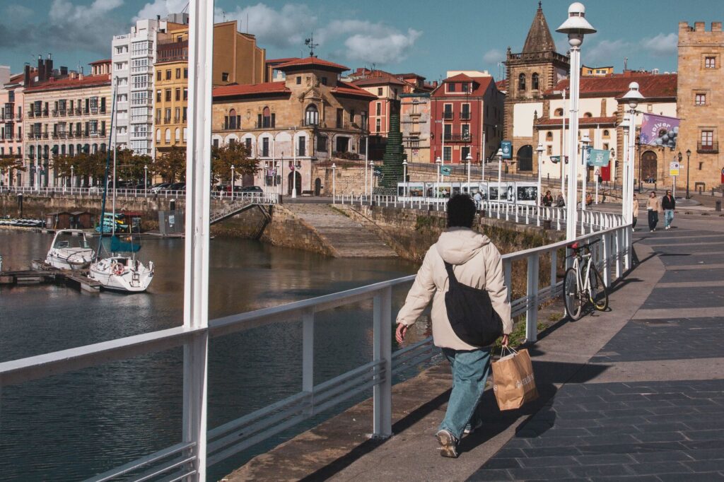 Vibrant street scene in Gijón, Spain featuring colorful architecture and a calm harbor.