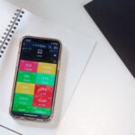 A smartphone displays a financial stock market app on a desk with a notebook and pencil.