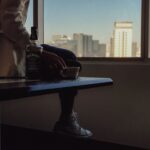 Adult sitting indoors holding a cup beside a bottle of Jack Daniel's, with urban skyline view.