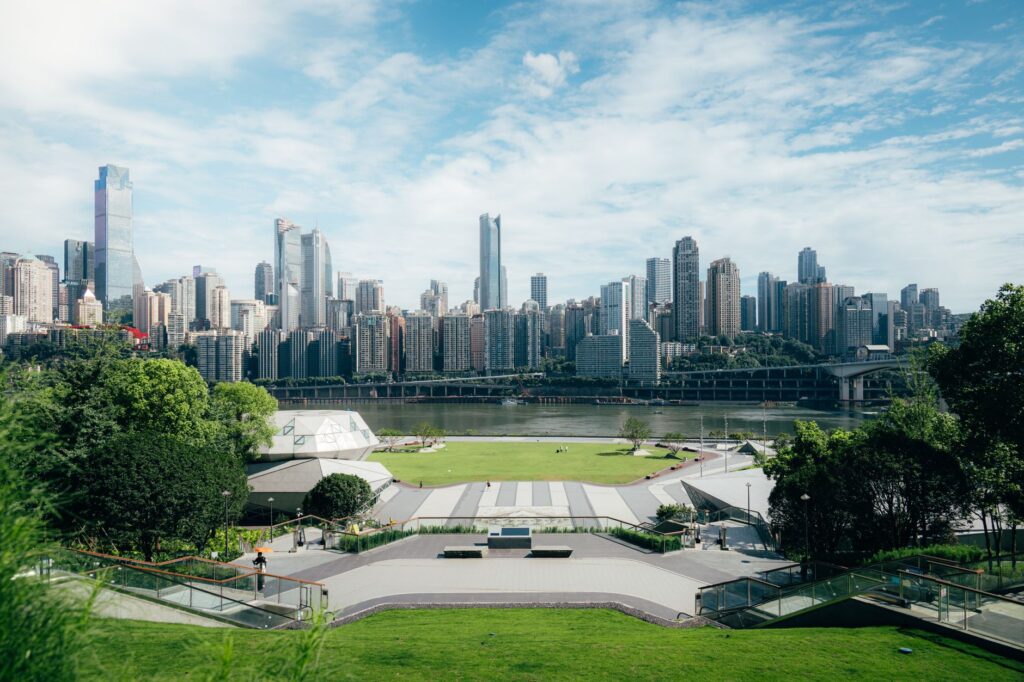 Wide cityscape view showcasing modern skyscrapers and a lush riverside park area under a clear sky.