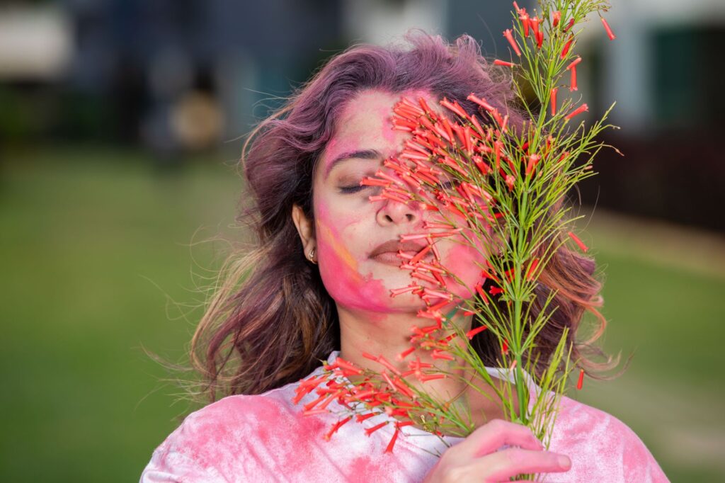 A woman joyfully celebrates Holi with vibrant colors and flowers outdoors.