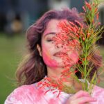A woman joyfully celebrates Holi with vibrant colors and flowers outdoors.