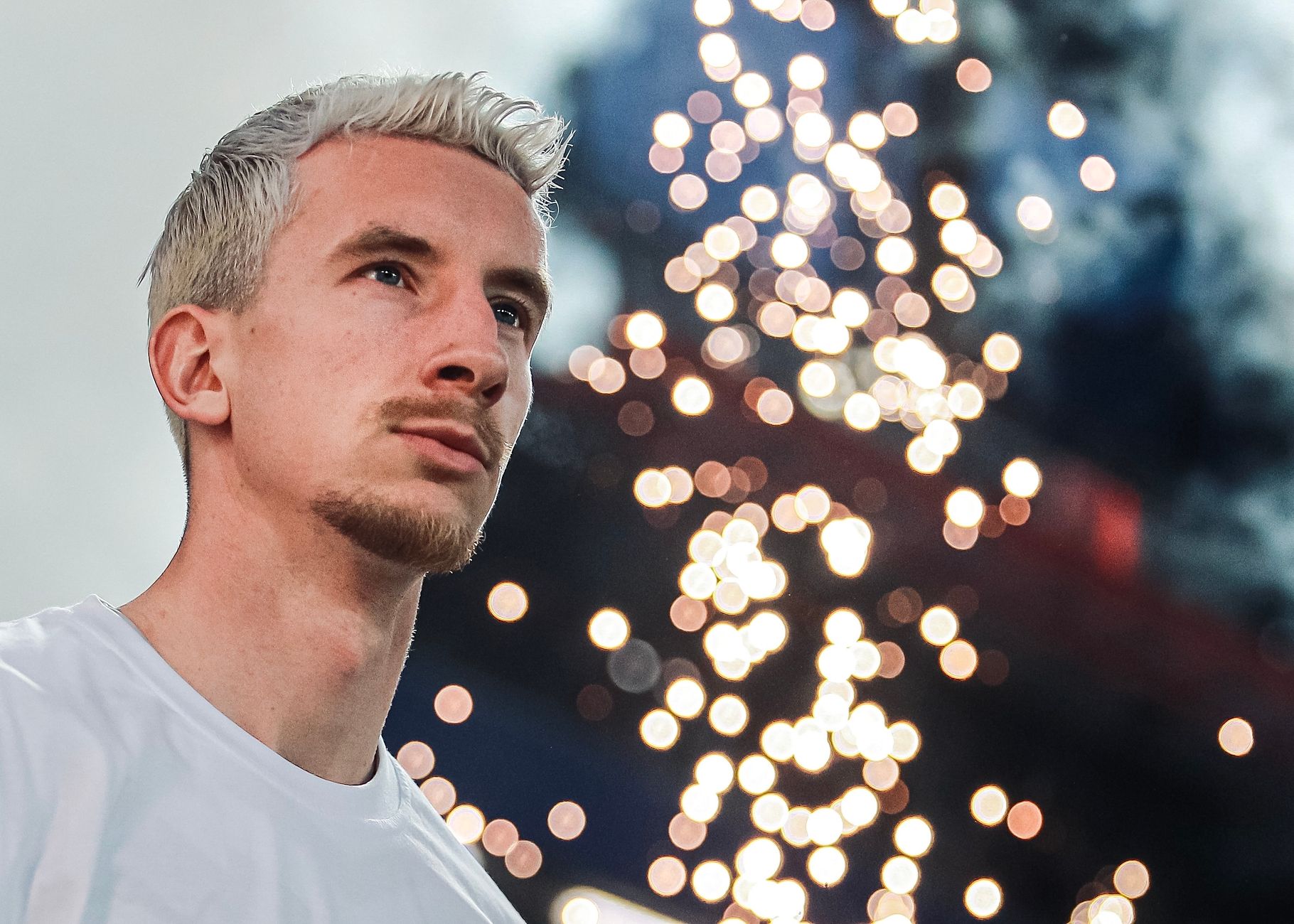 Portrait of a man with blonde hair gazing at festive lights in Moscow, Russia.