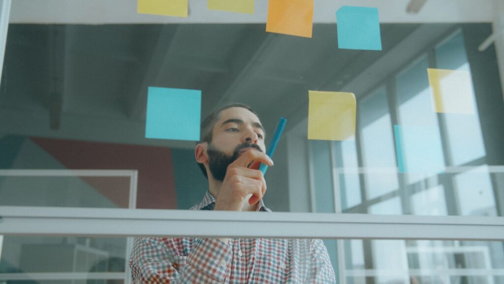 Focused businessman writing on sticky notes in a modern office setting, brainstorming ideas.