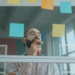 Focused businessman writing on sticky notes in a modern office setting, brainstorming ideas.