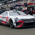 Toyota Camry race car with Sport Clips livery at a crowded racetrack, ready for action.