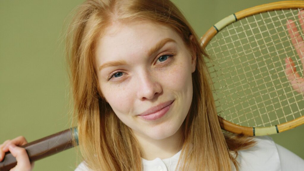 Close-up portrait of a young caucasian woman holding a squash racket against a green background.