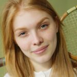 Close-up portrait of a young caucasian woman holding a squash racket against a green background.