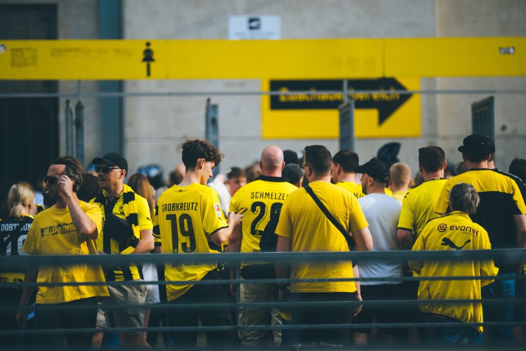 A vibrant crowd of football fans in yellow jerseys gathered at a stadium entrance during the day.