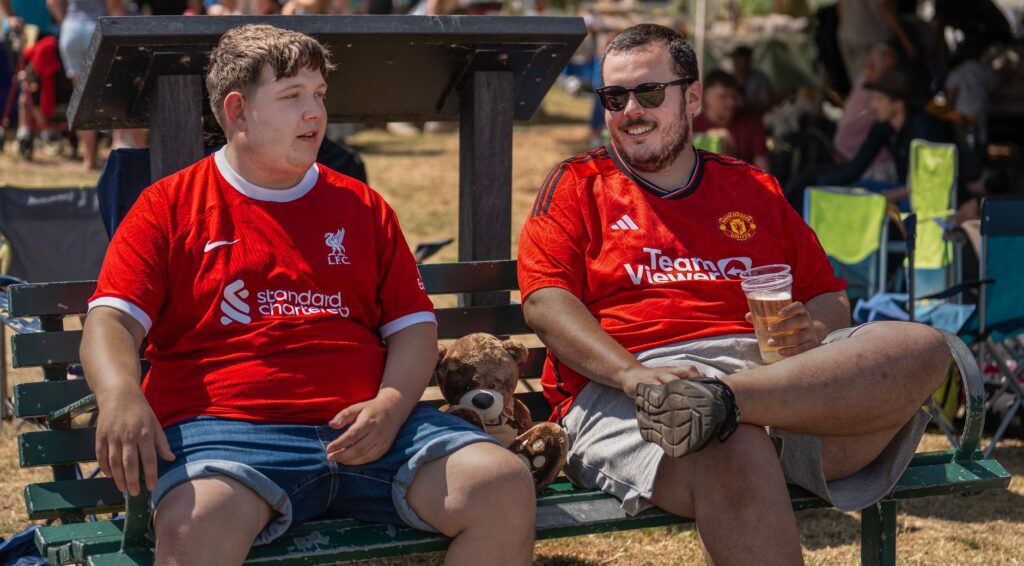 Two football fans wearing rival jerseys discussing at a public outdoor event.