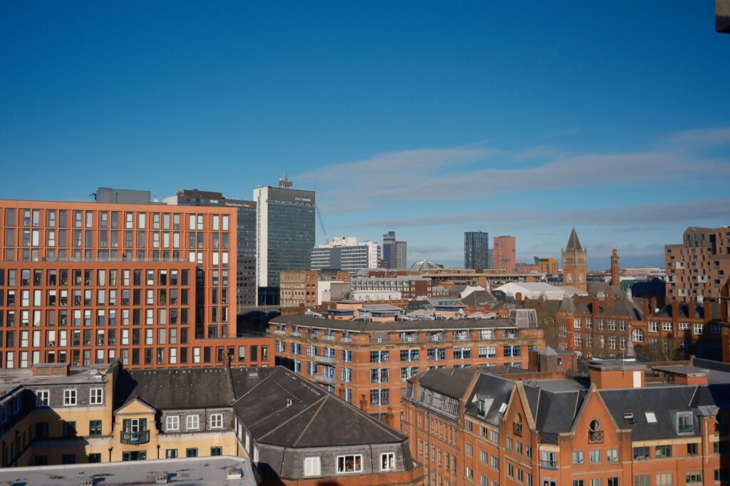 A vibrant cityscape of Manchester with modern and historical buildings under a clear blue sky.
