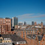 A vibrant cityscape of Manchester with modern and historical buildings under a clear blue sky.