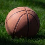 Close-up of a basketball resting on lush green grass, highlighting sports and recreation.