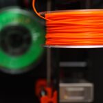 Detailed view of orange and green 3D printer filament spools, perfect for creative and industrial projects.