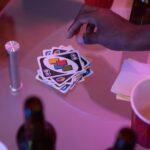 Close-up of a hand playing Uno cards on a table during a social gathering.