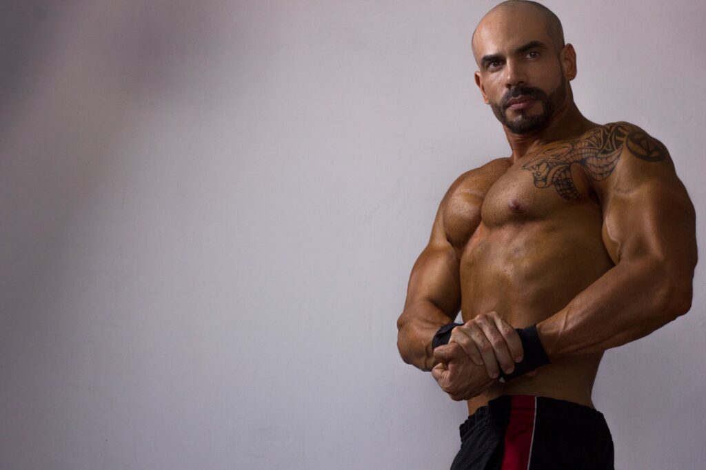 Strong, tattooed man flexing indoors, showcasing a powerful physique in Mexico.