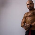 Strong, tattooed man flexing indoors, showcasing a powerful physique in Mexico.