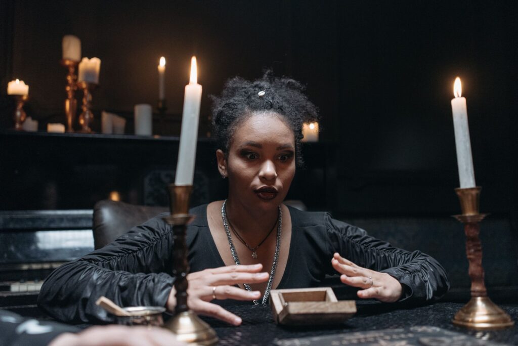 A medium surrounded by candles in a dark, mysterious setting, engaging in a seance.