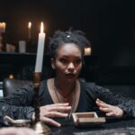 A medium surrounded by candles in a dark, mysterious setting, engaging in a seance.
