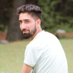 Portrait of a bearded man in white shirt looking over shoulder outdoors in Srinagar.