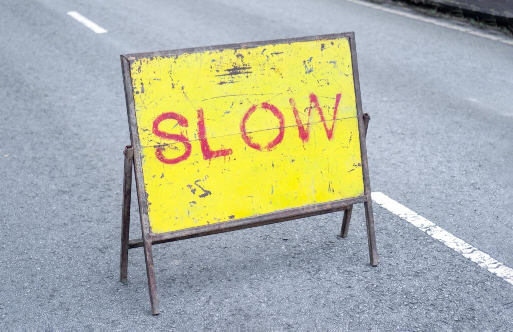 Aged yellow sign with 'SLOW' on an asphalt road, caution indicator.