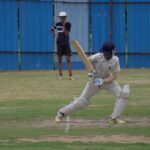 Cricket player batting on a grass field in Gahunje, India, showcasing dynamic sports action.