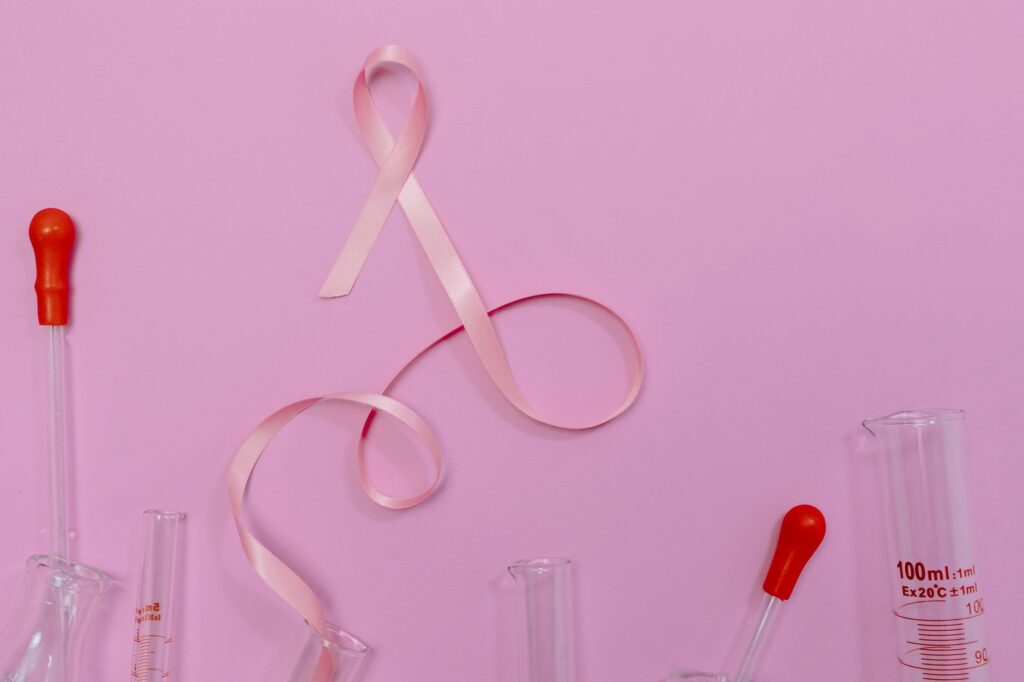 Pink ribbon symbolizing breast cancer awareness with laboratory glassware on a pink backdrop.
