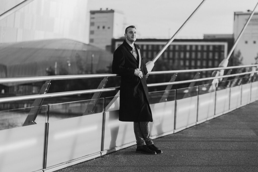 Elegant black and white portrait of a man on a modern bridge in Manchester, UK.