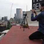 A photographer on a rooftop in Mexico City taking a photo of the skyline with a tripod and camera.