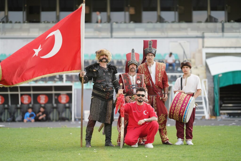 Group of men in traditional Turkish attire with a Turkish flag at a cultural event.