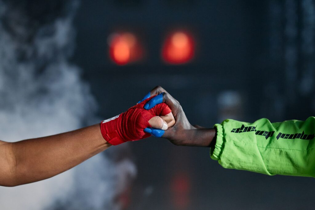 Close-up of two wrapped hands in a fist bump amid smoke, symbolizing unity in martial arts.