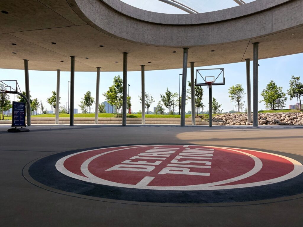 An outdoor basketball court featuring Detroit Pistons branding under a modern canopy.