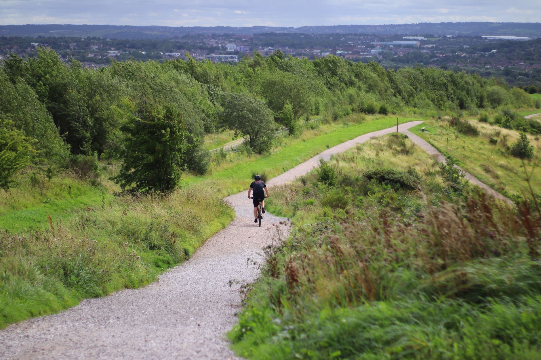 A cyclist rides down a winding path in the lush greenery of Silverdale, England.