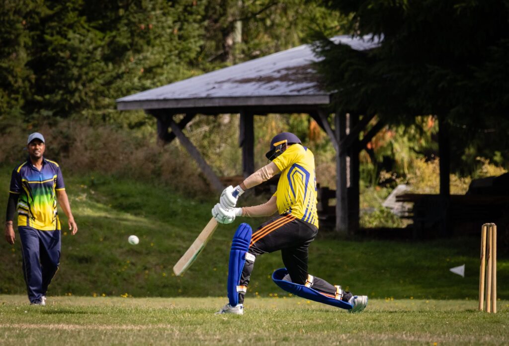 Cricketer batting an incoming ball outdoors on a sunny day.