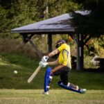 Cricketer batting an incoming ball outdoors on a sunny day.
