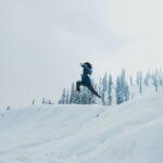 A man leaps across a snow-covered hillside against a backdrop of trees in Gulmarg.