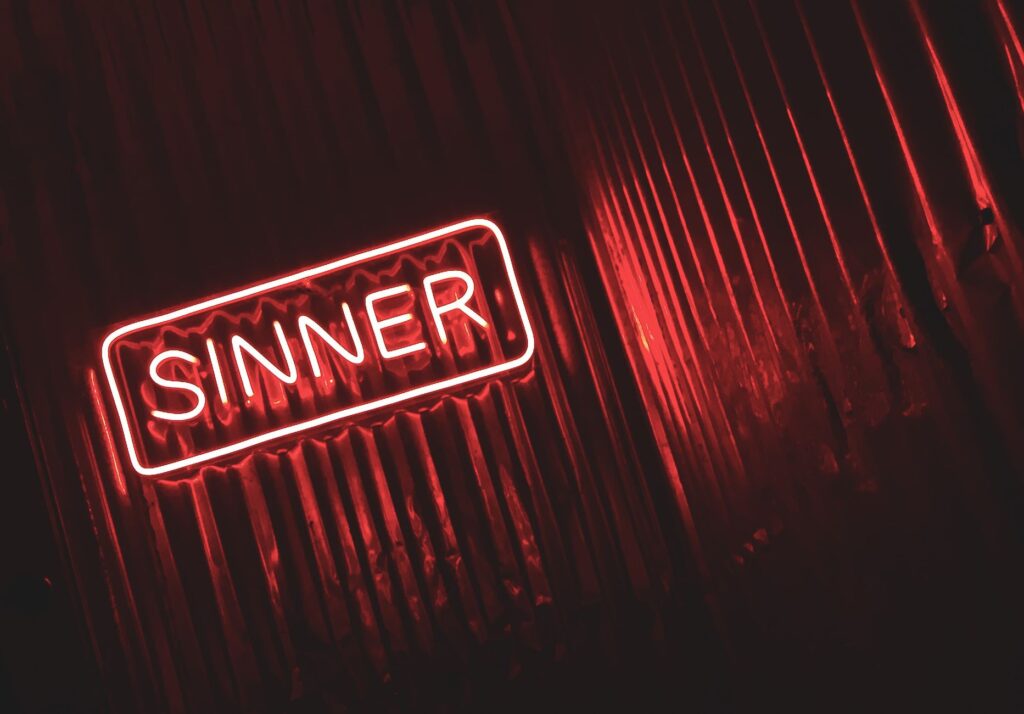 Bright red neon sign displaying the word 'SINNER' against a dark, moody background.