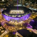 A vibrant night aerial view of Golden 1 Center in Sacramento, California during a lively event with a large crowd.