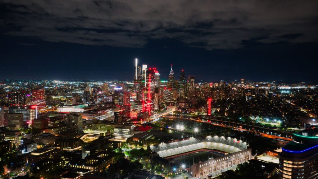 A breathtaking aerial view of Philadelphia's illuminated skyline at night, highlighting the vibrant cityscape and a prominent stadium.