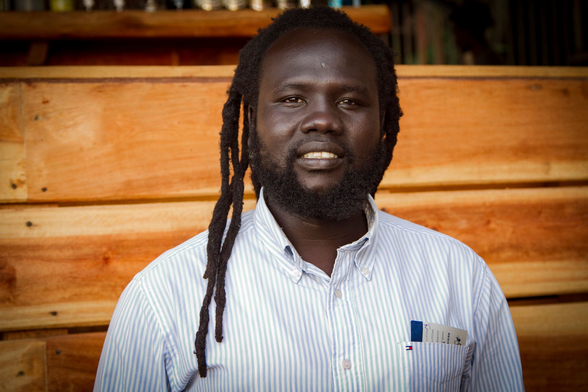 Close-up of a smiling man with dreadlocks and beard against a wooden background.
