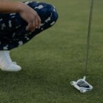 Golfer in patterned pants squatting with putter on grass ready to strike.