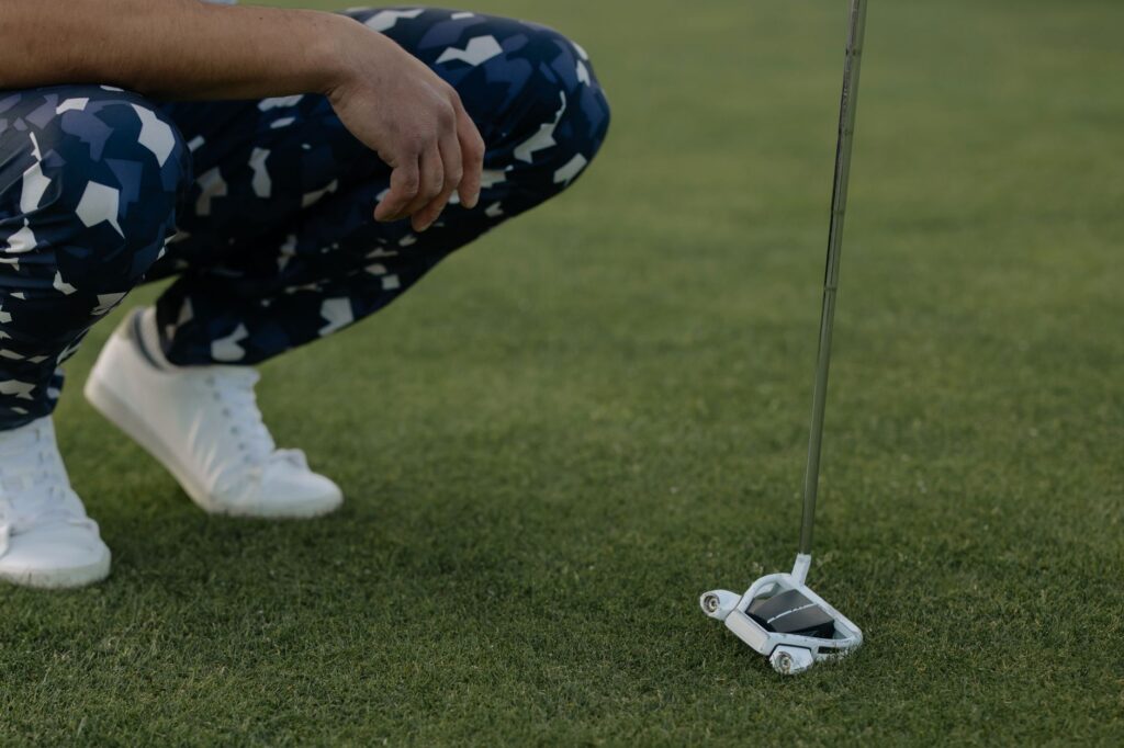 Golfer in patterned pants squatting with putter on grass ready to strike.