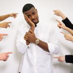A man in a white shirt looking stressed, surrounded by hands pointing at him.