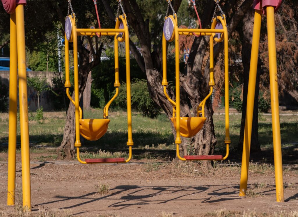 Two bright yellow and red swings in a quiet park in İzmir, Türkiye.